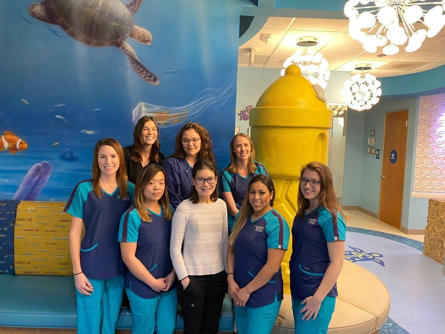 The team in matching blue scrubs in front of the office sea-turtle mural